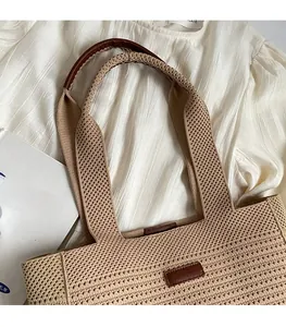 Detailed view of woven straw tote bag with brown leather handles on white fabric
