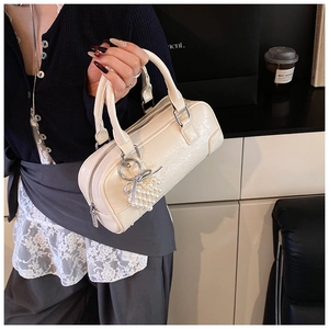Close-up of beige leather bowling bag with pearl heart charm and metallic zipper