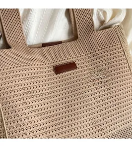 Close-up of light brown knitted tote bag featuring a diamond mesh pattern and leather logo tag