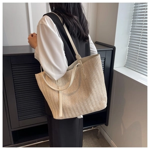 Detail view of woven straw tote bag featuring herringbone texture and slim leather straps