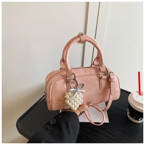 Detail of pink wrinkled leather Boston bag featuring a pearl heart charm and crossbody strap