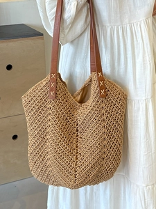 Minimalist woven straw tote bag with brown leather handles worn by a model in a white dress