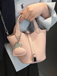 Pink litchi leather bucket bag with silver heart charm and lock detail held by model