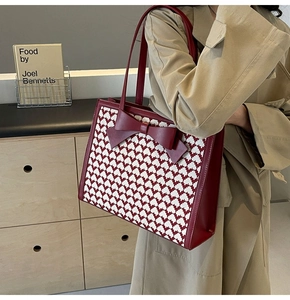 Detail of red bow tote bag with pixelated texture worn with a trench coat