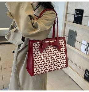Detail of red tote bag with bow decoration and woven heart pattern on camel coat