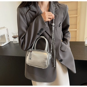 Mini borsa argento metallizzato con catena e ciondoli, indossata su blazer grigio