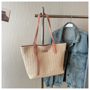Detail of woven straw tote bag with pink leather handles and branded plaque decoration