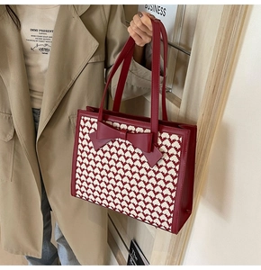 Detail of red bow accent on textured tote bag with contrast stitching and shoulder straps