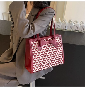 Detail of red tote bag with heart pattern and bow carried by model in professional suit