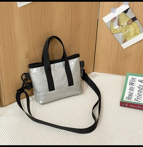 Detailaufnahme der silbernen Mini-Tasche mit schwarzen Griffen und Markenetikett
