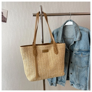 Detailed view of woven straw tote bag featuring herringbone pattern and brown leather handles