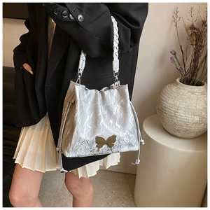 Detail of silver pleated bucket bag with gold butterfly accent and braided handle