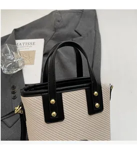 Détail de la texture tissée beige avec garniture en cuir noir et clous dorés sur le sac