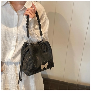 Detail of black drawstring bucket bag with silver butterfly charm and braided handle