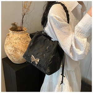 Detail of black pleated bucket bag featuring a silver butterfly buckle and braided strap