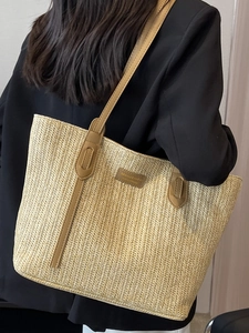 Large woven straw tote bag with brown leather handles worn by model in casual style
