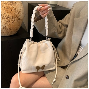 Detail of a beige drawstring bucket bag featuring a woven handle and golden butterfly hardware