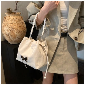 Close-up of cream-white drawstring bucket bag with braided handle and butterfly charm detail