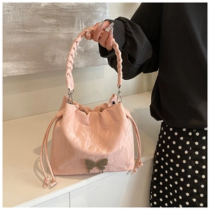 Detail of pink pleated bucket bag featuring metallic butterfly and woven handle