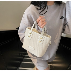 Détail d'un sac seau crème avec texture tissée, clous dorés et étiquette en cuir