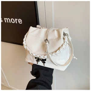 Detail of white pleated bucket bag with black butterfly charm and woven twisted handle