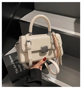 Detail of cream crossbody bag featuring glossy finish, silver lock and colorful woven charm