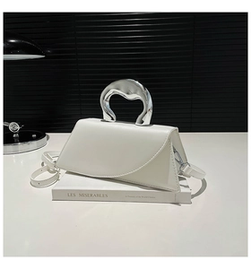 Détail du sac à main trapèze blanc avec poignée en métal argenté sur fond noir élégant