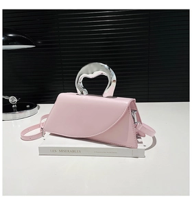 Détail d'un sac trapèze rose avec poignée unique en métal liquide argenté sur un livre
