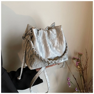 Detail of silver pleated bucket bag with metallic texture and gold butterfly hardware