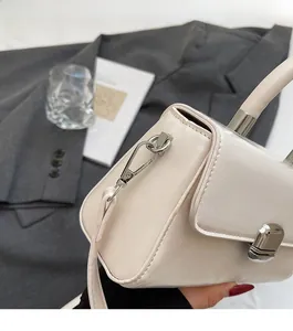 Detail of a creamy beige square crossbody bag with silver metal lock and leather texture