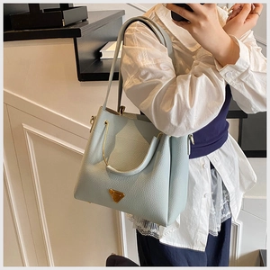 Macro detail of a light blue lychee pattern leather tote bag with gold metal logo and handle