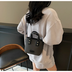 Vue latérale du sac seau noir avec texture tissée et détails de clous dorés sur modèle