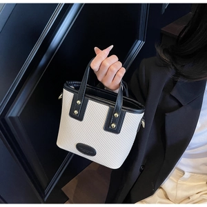 Détail d'un sac seau tissé beige avec garniture en cuir noir et clous en métal doré