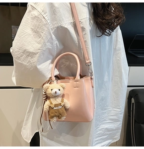 Detail view of pink leather bucket bag featuring a cute teddy bear charm and sleek handles