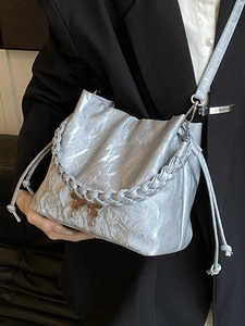 Silver pleated bucket bag with twisted handle and gold butterfly clasp on black suit