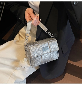 Detailansicht einer silbernen geflochtenen Handtasche mit Kette und weißem Bommelanhänger