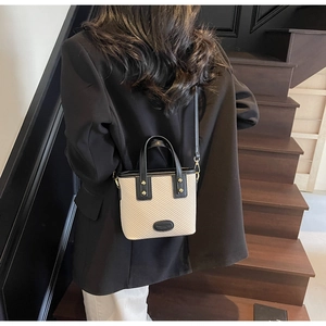 Détail du sac seau bicolore beige texturé avec bandoulière en cuir noir sur un mannequin