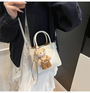 Detail of white faux leather bucket bag with brown teddy bear charm on model shoulder