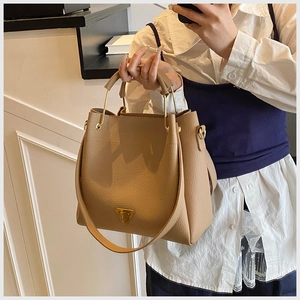 Detail view of khaki lychee textured bucket bag with gold triangle buckle and handle