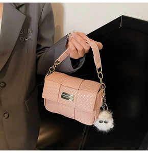 Detail der rosa geflochtenen Handtasche mit goldener Kette und weißem Plüsch-Pompon-Anhänger