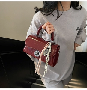 Détail d'un sac à main en cuir verni bordeaux avec fermoir argenté porté par un mannequin