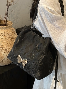 Elegant black pleated bucket bag with a large silver butterfly buckle shown on model
