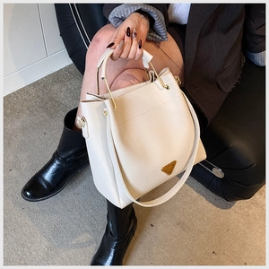 Detail of lychee pattern leather bucket bag featuring a golden circular handle and metal logo