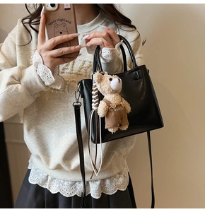 Detail of a black leather bucket bag featuring a cute plush bear charm with brown strap