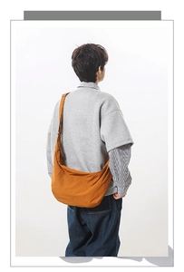 Rear view of a bright orange nylon crescent bag worn crossbody by a model on plain white background