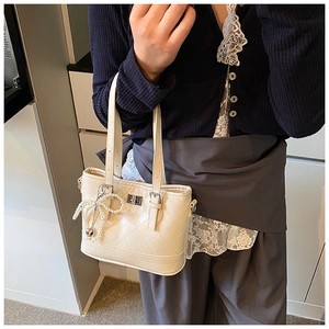 Close-up of white quilted bucket bag with pearl bow charm and silver metal lock