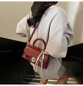 Détail du sac bandoulière en cuir verni bordeaux avec fermoir rotatif et breloque tissée