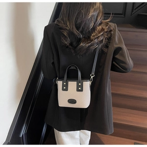 Détail du sac seau bicolore en tissage et cuir porté avec un blazer noir et un pantalon blanc