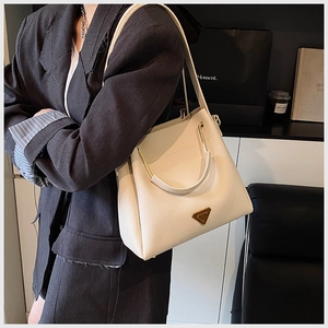 Detail of cream lychee texture handbag with golden triangle metal plaque and strap