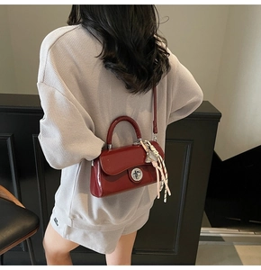 Sac à main en cuir verni bordeaux avec fermoir rotatif argenté porté par un mannequin